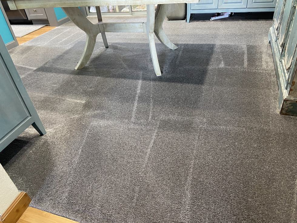 A cleaned living room carpet with fresh vacuum lines running across it under a dining table.